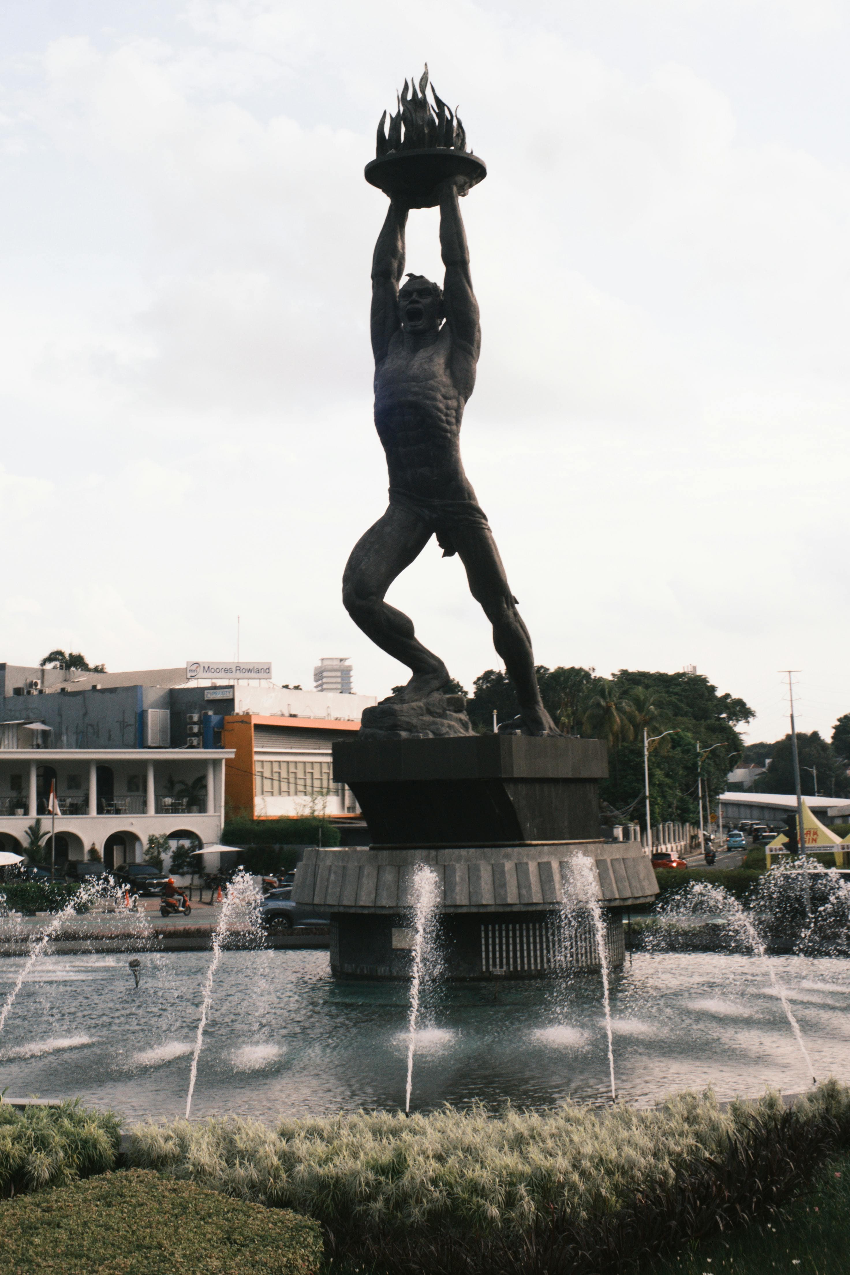 Bronze statue of a man holding a flaming dish overhead, standing above a fountain roundabout in Jakarta.
